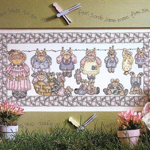 以下が含まれることがあります： 「One, two, loads to do. Three, four, Scrub some more. Five, six, hang them quick.」というテキストが書かれた、洗濯ロープにぶら下がっているテディベアを並べたクロスステッチパターンです。