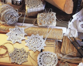 May include: A collection of silver crocheted snowflakes, some with a string attached, on a table with brown paper, gold wrapping paper, and other craft supplies.