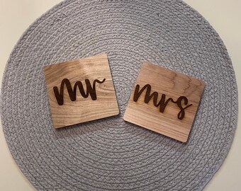 Op de afbeelding: Twee houten borden met de woorden "mr" en "mrs" erop gegraveerd. De borden liggen op een grijze ronde placemat.