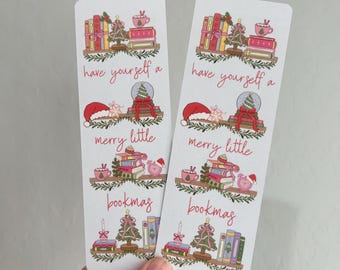 May include: Two rectangular bookmarks with a festive design. Each bookmark features illustrations of books, Christmas trees, snow globes, and Santa hats. The text "have yourself a merry little bookmas" is written in cursive.
