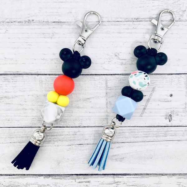Könnte beinhalten: Zwei schwarze und weiße Perlen-Schlüsselanhänger mit schwarzen Mickey-Maus-Ohren und Quasten. Ein Schlüsselanhänger hat rote, gelbe und weiße Perlen. Der andere Schlüsselanhänger hat blaue, weiße und schwarze Perlen.
