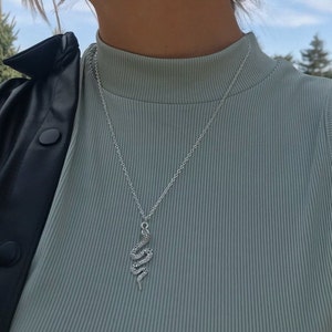 May include: A silver snake necklace with a delicate chain. The necklace is worn by a person wearing a light blue ribbed tank top and a black leather jacket.