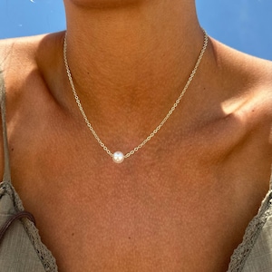 May include: A simple gold chain necklace with a single white pearl pendant.
