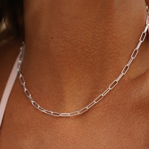 May include: A silver chain necklace with a delicate, linked design. The chain is made of small, rectangular links.