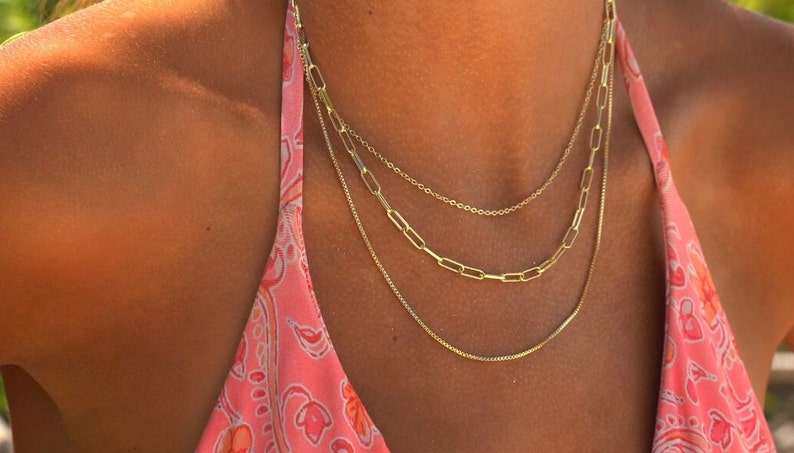 Beach multi chain jewelry set. Necklaces displayed at the ocean, 3 separate chains come with this purchase. Each necklace varies in thickness for the perfect multi-chain choker set. The gold is 14k and long lasting.