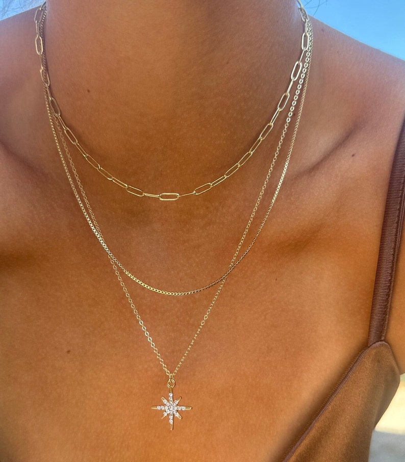 three layer stacking14k gold chain necklace. The first chain is a  thick paperclip chain, the second is a snake box chain and finally a cable chain with a diamond North Star pendant.