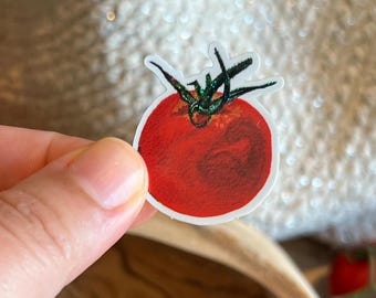 May include: A die-cut sticker featuring a round, vibrant red tomato with a textured, painterly appearance. The tomato has a dark green, glittery stem and leaves at the top, all outlined with a thin white border against a neutral background.