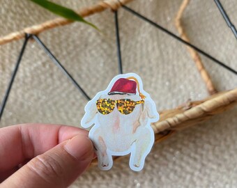 May include: A white turkey wearing a red fez and sunglasses with gold glitter accents. The turkey is wearing a festive hat and sunglasses.