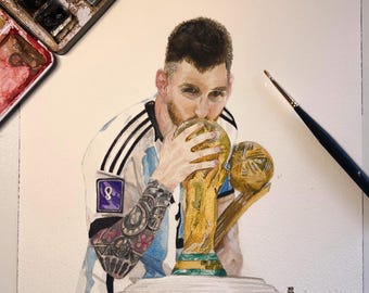 May include: A watercolor painting of a soccer player in a white and light blue jersey with the number 8, kissing a gold trophy. The player has dark hair, a beard, and tattoos on the arm. A paintbrush and a paint palette are visible nearby.
