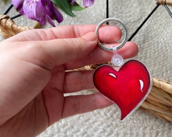 May include: A red heart-shaped keychain with a silver ring. The heart is made of clear plastic with a red heart design inside.