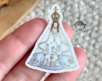 May include: A die-cut sticker featuring a stylized illustration of a figure wearing a white and gold gown with intricate floral embroidery, a tall crown, and a delicate necklace. The text DOT secret is printed in black near the upper right edge.