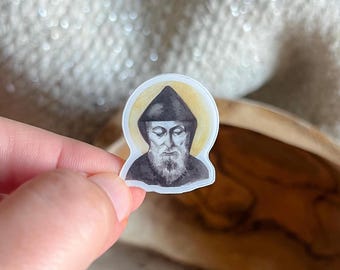 May include: A die-cut sticker featuring a detailed illustration of a monk with a long beard wearing a dark hooded robe. The figure is set against a soft, circular yellow halo background, rendered in a style reminiscent of a watercolor painting.