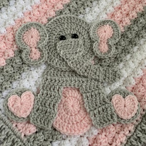 May include: A gray crocheted elephant applique with pink ears, feet, and a nose. The elephant is on a pink, white, and gray striped crocheted blanket.