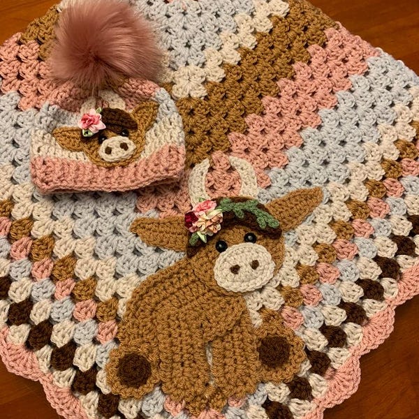May include: A crocheted baby blanket with a brown cow applique and a matching crocheted hat with a pink pom-pom.