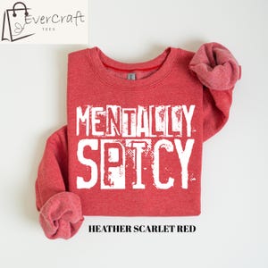Peut inclure: Sweat-shirt rouge avec l'inscription blanche "MENTALLY SPICY". Le sweat-shirt a un col rond et des manches longues. Le texte "Heather Scarlet Red" est imprim&eacute; en dessous.