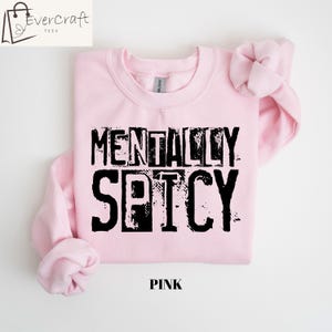 Peut inclure: Un sweat-shirt rose clair avec l'inscription noire "MENTALLY SPICY" dans une police de caract&egrave;res vieillie. Le mot "PINK" est imprim&eacute; en noir en bas. Le logo Evercraft Tees est dans le coin sup&eacute;rieur gauche.