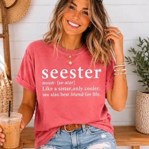 May include: A coral-colored t-shirt with the word "seester" in white block letters. The text below defines "seester" as "Like a sister, only cooler. See also best friend for life."