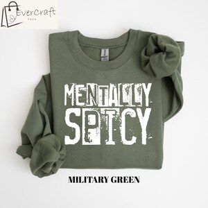 Peut inclure: Sweat-shirt vert militaire avec l'inscription blanche &laquo; MENTALLY SPICY &raquo;. Le sweat-shirt &agrave; col rond a des manches longues. La marque &laquo; Evercraft Tees &raquo; est dans le coin sup&eacute;rieur gauche. Le bas de l'image indique &laquo; MILITARY GREEN &raquo;.