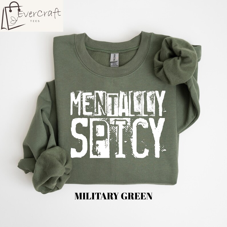 Peut inclure: Sweat-shirt vert militaire avec l'inscription blanche &laquo; MENTALLY SPICY &raquo;. Le sweat-shirt &agrave; col rond a des manches longues. La marque &laquo; Evercraft Tees &raquo; est dans le coin sup&eacute;rieur gauche. Le bas de l'image indique &laquo; MILITARY GREEN &raquo;.