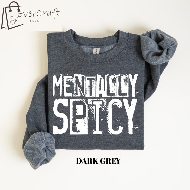 Peut inclure: Sweat-shirt gris fonc&eacute; avec l'inscription "MENTALLY SPICY" en grandes lettres blanches. Le texte "DARK GREY" est imprim&eacute; en dessous. Le sweat-shirt a un col rond et des manches retrouss&eacute;es.