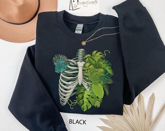 May include: Black sweatshirt with a graphic print of a human ribcage with green leaves growing from it. The text "BLACK" is printed on the bottom of the sweatshirt.