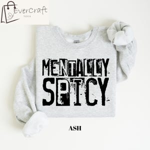 Peut inclure: Sweat-shirt gris clair avec l'inscription noire "MENTALLY SPICY". Le mot "ASH" est imprim&eacute; en dessous. Le sweat-shirt a un col rond et des manches longues.