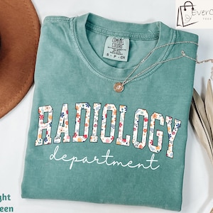 May include: Light green t-shirt with a floral print design that says "RADIOLOGY department" in white text.