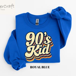 May include: A royal blue sweatshirt with the text "90's Kid" in a retro, rainbow-colored font.
