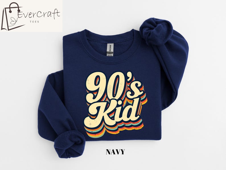 May include: A navy blue sweatshirt with a retro-style graphic that says "90's Kid" in yellow and orange letters. The sweatshirt is a crew neck style.
