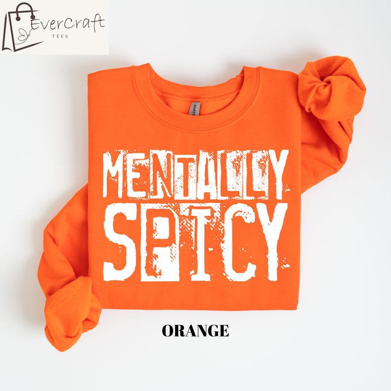 Peut inclure: Un sweat-shirt orange avec les mots "MENTALLY SPICY" en blanc, avec des lettres us&eacute;es. Le mot "ORANGE" est imprim&eacute; en gras, en police sans-serif en bas du sweat-shirt. Le logo Evercraft Tees est dans le coin sup&eacute;rieur gauche.