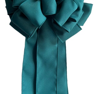 May include: A large, teal-colored decorative bow with multiple loops and long, flowing tails. The bow is made of a smooth, satin-like material, perfect for holiday decorations or gift wrapping. The bow's design is full and voluminous.