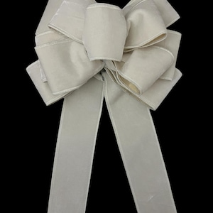 May include: A large, ivory white velvet bow with two long tails. The bow is tied in a classic, symmetrical style.
