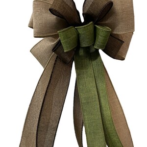Op de afbeelding: Een grote, decoratieve strik gemaakt van drie verschillende linten. De strik is gemaakt van een bruin en beige lint, een groen lint en een bruin lint met een zwarte rand. De strik is gebonden met een lus en linten.