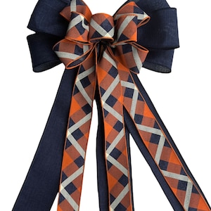 May include: A large bow made with navy blue and orange plaid ribbon. The bow has three tails and is tied with a navy blue ribbon.