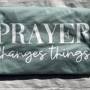 May include: A teal blue t-shirt with the text "PRAYER Changes things" printed in white.