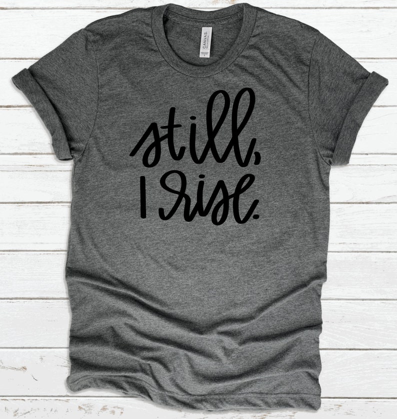 May include: A heather gray t-shirt with the text "still, I rise" printed in black.