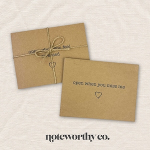 May include: Two brown kraft paper envelopes with handwritten messages. The top envelope says "open when you feel stressed" and the bottom envelope says "open when you miss me". Both envelopes have a small heart drawn on them. The envelopes are tied together with twine. The text "noteworthy co." is printed below the envelopes.
