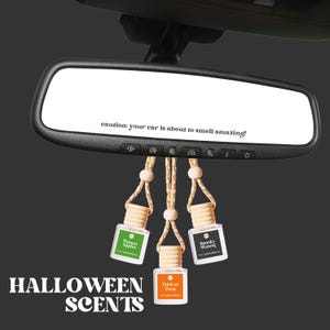 May include: A car rearview mirror with the text "caution: your car is about to smell amazing!" and three hanging air fresheners. The air fresheners are labeled "Poison Apples", "Trick or Treat", and "Spooky Season". The words "HALLOWEEN SCENTS" are at the bottom.
