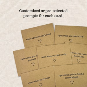 May include: A set of six brown cards with different prompts written on them. Each card has a small heart symbol at the bottom. The prompts are: "open when you can't sleep", "open when you need a hug", "open when you do yourself", "open when you feel lonely", "when you need motivation", "open when you're sick", and "open when you're feeling overwhelmed".