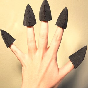 May include: Five black foam claw-shaped finger covers, each featuring a pointed tip and a vertical seam detail running down the centre. These conical accessories are designed to fit over the fingertips, creating a sharp, claw-like appearance.