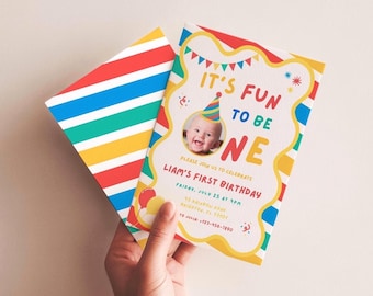 May include: A colorful birthday invitation with the text "IT'S FUN TO BE ONE" and a photo of a baby wearing a party hat. The invitation has a yellow border and a matching envelope with rainbow stripes.