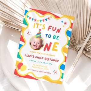 K&ouml;nnte beinhalten: Eine farbenfrohe Geburtstagseinladung mit dem Text "IT'S FUN TO BE ONE" und einem Foto eines Babys mit Partyhut. Die Einladung enth&auml;lt Details f&uuml;r Liams ersten Geburtstag, mit Luftballons und Konfetti.