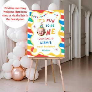 K&ouml;nnte beinhalten: Ein farbenfrohes Geburtstags-Schild auf einer Staffelei. Es zeigt "It's Fun to be One" mit einem Babyfoto, "Welcome to Liam's First Birthday" und das Datum 05.05.2026. Verziert mit Luftballons und einer Partyh&uuml;tchen, ideal f&uuml;r den ersten Geburtstag.