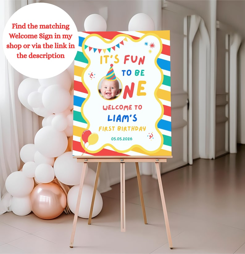 K&ouml;nnte beinhalten: Ein farbenfrohes Geburtstags-Schild auf einer Staffelei. Es zeigt "It's Fun to be One" mit einem Babyfoto, "Welcome to Liam's First Birthday" und das Datum 05.05.2026. Verziert mit Luftballons und einer Partyh&uuml;tchen, ideal f&uuml;r den ersten Geburtstag.