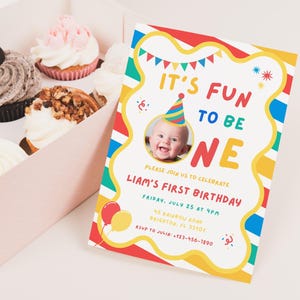 K&ouml;nnte beinhalten: Eine farbenfrohe Geburtstagseinladung mit dem Text "IT'S FUN TO BE ONE" und einem Foto eines Babys mit Partyhut. Die Einladung ist mit roten, gelben, blauen und gr&uuml;nen Streifen verziert und enth&auml;lt Party-Details. Cupcakes befinden sich in einer rosa Schachtel.