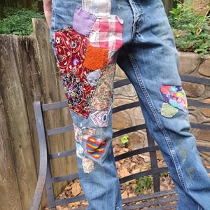 May include: Blue denim jeans with multiple colourful fabric patches sewn on the front of the legs.