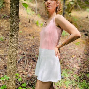 May include: A pink and white knitted dress with a sleeveless design. The dress has a fitted bodice and a flared skirt.