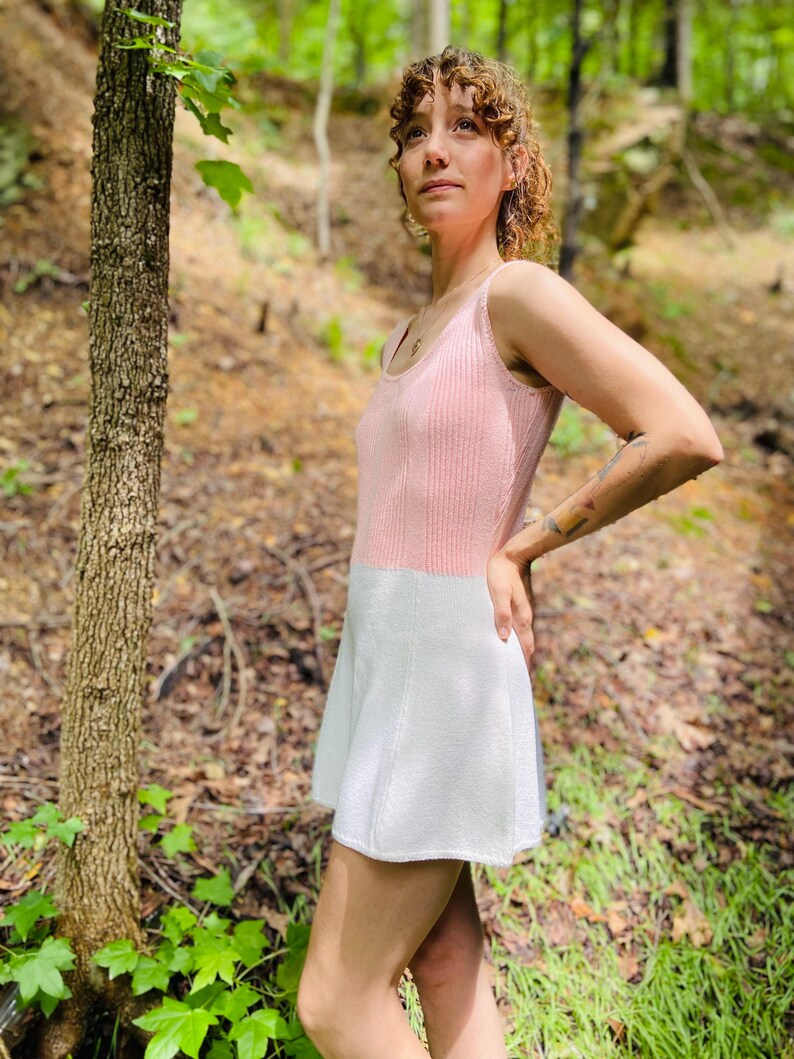 May include: A pink and white knitted dress with a sleeveless design. The dress has a fitted bodice and a flared skirt.