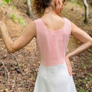 May include: A pink and white knitted dress with a sleeveless design. The dress has a fitted bodice and a flared skirt.