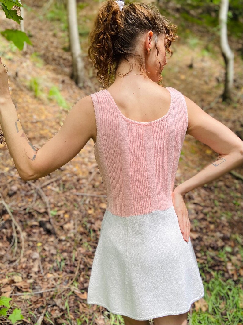 May include: A pink and white knitted dress with a sleeveless design. The dress has a fitted bodice and a flared skirt.